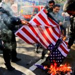 Group burning American flag on street pavement