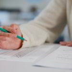 Person holding pencil over exam paper on table