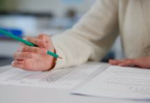 Person holding pencil over exam paper on table