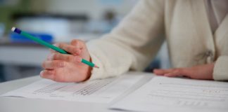 Person holding pencil over exam paper on table