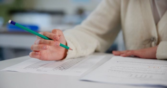 Person holding pencil over exam paper on table