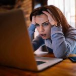 Woman frustrated at laptop, holding her head