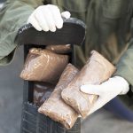 Person handling packages wearing gloves and green jacket.