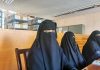Three women in niqabs seated in a library.