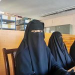 Three women in niqabs seated in a library.