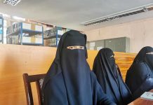 Three women in niqabs seated in a library.