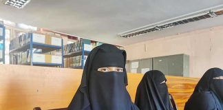 Three women in niqabs seated in a library.