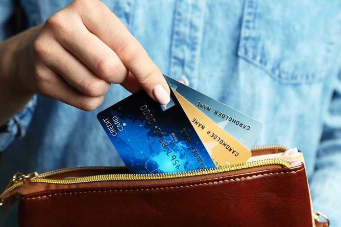 Hand holding credit cards over a brown purse