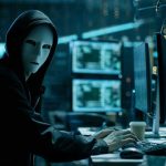 Person wearing mask and hoodie at computer desk