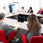 A diverse group of professionals engaged in a meeting with a presenter at a whiteboard