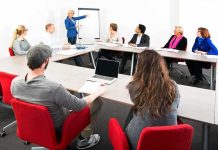 A diverse group of professionals engaged in a meeting with a presenter at a whiteboard