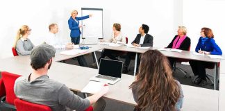 A diverse group of professionals engaged in a meeting with a presenter at a whiteboard