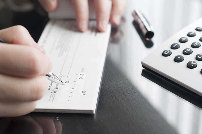 shutterstock_200867021.jpg Person writing a check on a reflective surface with a calculator nearby