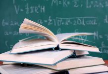 A stack of books with one open on top in front of a chalkboard filled with mathematical equation