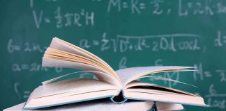A stack of books with one open on top in front of a chalkboard filled with mathematical equation