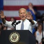 A man speaks at podium with raised hands.