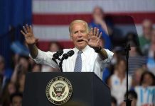 A man speaks at podium with raised hands.