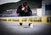 Crime scene photographer behind police tape with evidence marker