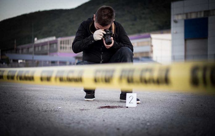 702059647 Crime scene photographer behind police tape with evidence marker