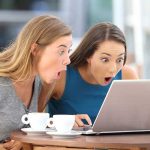 Two women surprised while looking at a laptop.