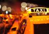Close-up of a taxi sign illuminated at night with blurred city lights in the background