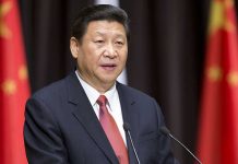 A political leader delivering a speech at a podium with national flags in the background