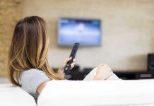 A woman sitting on a sofa, holding a remote control and watching television