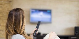 A woman sitting on a sofa, holding a remote control and watching television