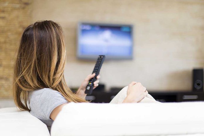 shutterstock_243577255.jpg A woman sitting on a sofa, holding a remote control and watching television
