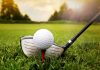 A golf ball on a tee with a golf club resting beside it on green grass