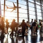 Crowd of travelers in airport terminal with airplane outside.