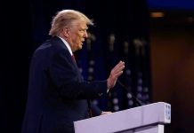 Trump DEMANDS $230M – Turns to Taxpayers Person speaking at a podium with hand raised