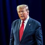 Trump Frees Convicted Felon—Washington Erupts Man in suit with red tie speaking on stage.