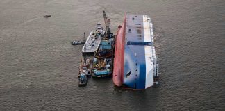 Capsized ship with cranes and tugboats around it.