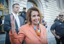 Pelosi Exit Sparks CHAOS: Rat Race Begins Woman in orange blazer speaking, surrounded by security personnel.