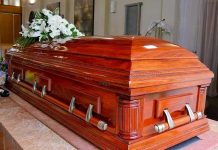 Funeral Home Horror—190 Bodies Hidden, Families Deceived Wooden casket with white flowers in a funeral home.