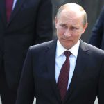 Putin BLASTS Kyiv – Nobody Warned Civilians! A serious-looking man in a suit walking outdoors with security personnel in the background