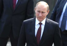 Putin BLASTS Kyiv – Nobody Warned Civilians! A serious-looking man in a suit walking outdoors with security personnel in the background