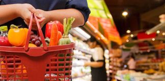 Person holding a basket filled with colorful vegetables in a supermarket