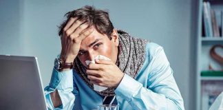 Man with tissue feeling unwell at laptop desk