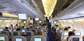 Interior view of an airplane with passengers seated and using in-flight entertainment screens