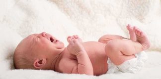 A newborn baby lying on a soft blanket, crying with a distressed expression