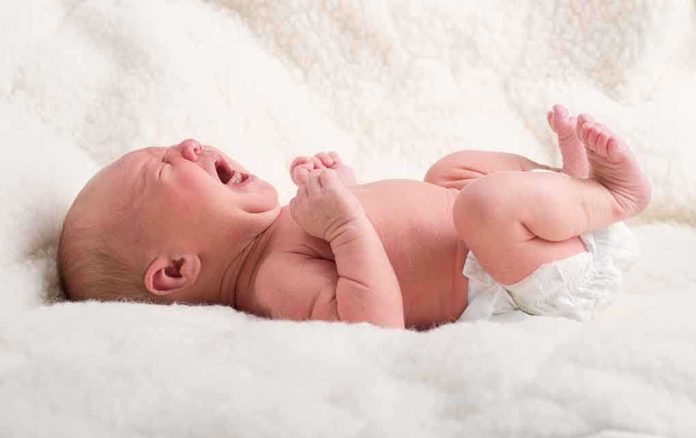 shutterstock_154248668.jpg A newborn baby lying on a soft blanket, crying with a distressed expression