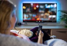 Paramount’s Bold Move: Warner Bros. Takeover Attempt Person sitting on a couch watching a movie on a TV with popcorn in hand