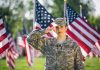 Soldier saluting in front of American flags outdoors.
