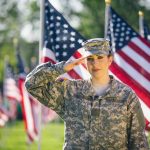 Soldier saluting in front of American flags outdoors.
