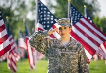 Soldier saluting in front of American flags outdoors.
