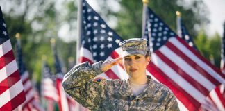 Soldier saluting in front of American flags outdoors.