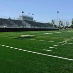 Empty football field with bleachers in background.