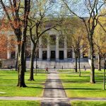 Students walking on a university campus with autumn trees and a historic building in the background